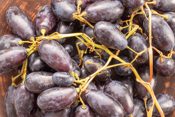 One bunch of juicy organic black grapes on a clay plate, close-up, top view.
