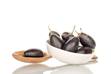 Several berries of black grapes in a white saucer with a wooden spoon, close-up, isolated on white.