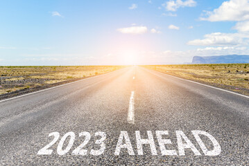 New year 2023 ahead. Conceptual empty straight road in a flat landscape with the phrase "2023 AHEAD" painted on asphalt.