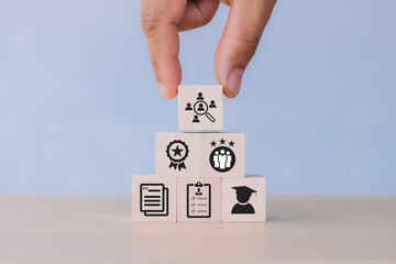 Job search, headhunting and recruitment process. Holding wooden cubes with icons of education, qualification, cv, resume, skills and experience on smart grey background. HRM and recriutement concept.