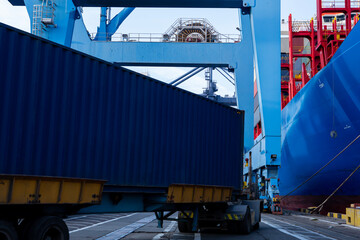 Port container terminal with a container ship in the background and a blue container in the foreground