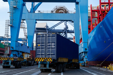 Port container terminal with a container ship in the background and a blue container in the foreground