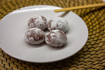 Wooden chopsticks and traditional Japanese dessert mochi or daifuku in rice dough. Four mochi ice cream balls on white round plate on brown rattan doily. Asian sweet delicious food dessert top view.