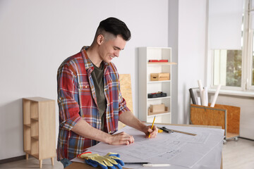 Young handyman working with blueprints at table in room