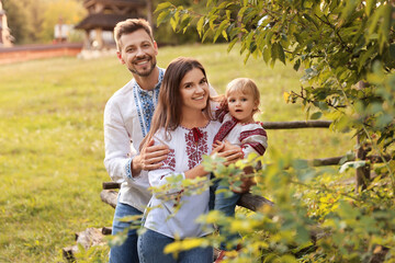 Happy cute family in embroidered Ukrainian shirts near rustic fence on sunny day