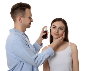 Man spraying medication into woman`s ear on white background