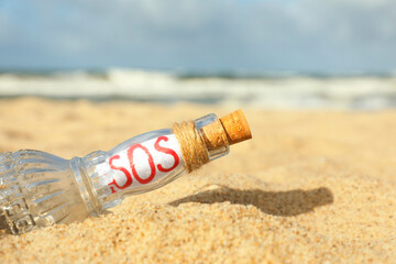 Fototapeta na wymiar Glass bottle with SOS message on sand near sea, closeup
