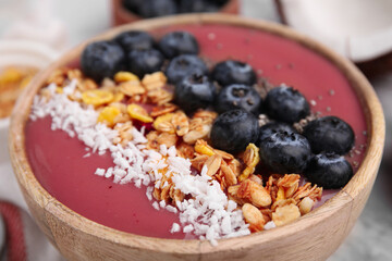 Bowl of delicious fruit smoothie with fresh blueberries, granola and coconut flakes on white marble table, closeup