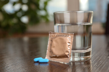 Glass of water, condom and pills on wooden table indoors, closeup with space for text. Potency problem concept