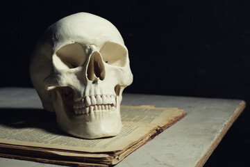 Human skull and old book on table against black background, space for text