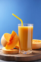 Tasty pumpkin juice in glass and cut pumpkin on light grey table against blue background