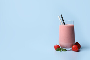 Glass with delicious berry smoothie and fresh strawberries on light blue background. Space for text
