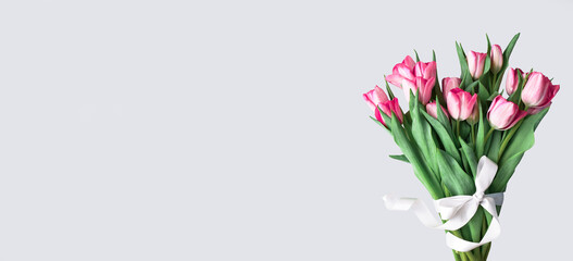 Pink tulips bouquet tied with white satin ribbon on gray background