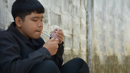 Boy learning to smoke by himself in the area behind the school fence which is a hidden place for...
