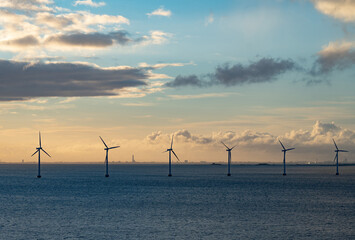 Wind farm in the open sea during sunset. Offshore wind generators. Renewable and green energy concept.