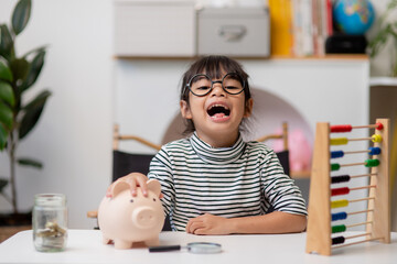 Little Asian girl saving money in a piggy bank, learning about saving, Kid save money for future...