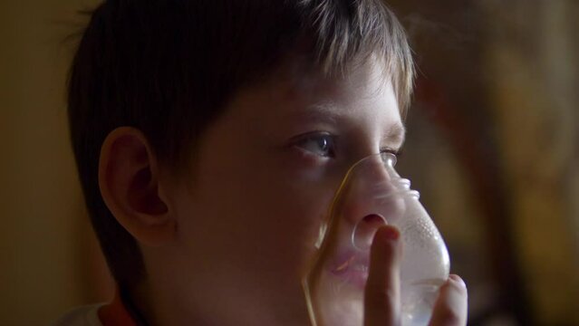 a sad child is treated by breathing in a mask with inhalations. treatment of allergy cough by inhalation. boy at home breathing in a mask with an inhaler