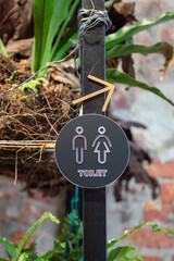Toilet signage showing male and female symbol with arrow and foliage background