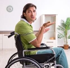 Young male invalid in wheel-chair suffering at home