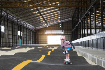 asian child skater or kid girl fun playing skateboard or ride surf skate in indoor pump track in skate park by extreme sports surfing to wearing helmet elbow pads wrist knee support for body safety