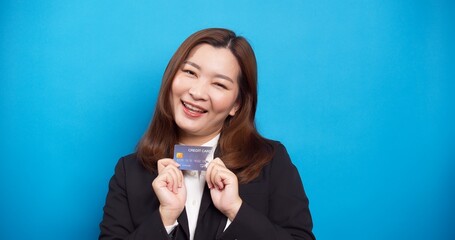 Beautiful Asian businesswoman in black suit holding credit card with a smile in the studio shot on blue background