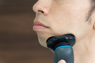 電気シェーバーで髭を剃る30代の男性