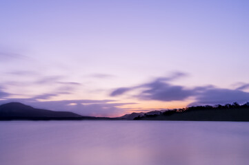 薄い紫色の夜明けの空の色を水面に反射する湖。