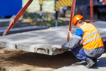 Slinger lays concrete slab on construction site on summer day. Worker in protective vest and...