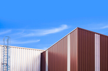 Corrugated steel wall of 2 warehouse buildings with metal stair against blue sky background in low angle view
