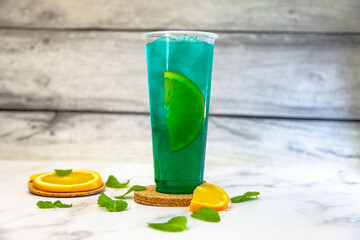 Lemonade with ice and a turquoise orange slice in a large plastic glass