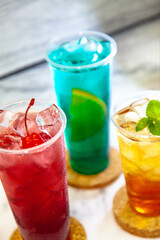 Three juicy lemonades of different colors in transparent plastic glasses with ice
