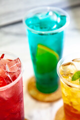 Three juicy lemonades of different colors in transparent plastic glasses with ice