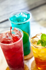 Three juicy lemonades of different colors in transparent plastic glasses with ice