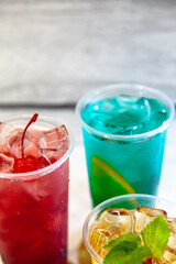 Three juicy lemonades of different colors in transparent plastic glasses with ice