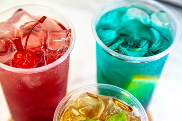 Three juicy lemonades of different colors in transparent plastic glasses with ice