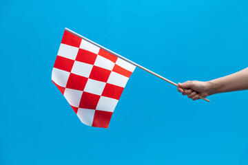 Human hand waving checkered flag on blue background