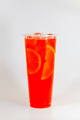 Red lemonade with ice and orange slices in a tall glass on a white background