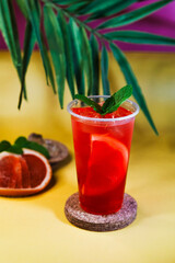 Red lemonade with grapefruit, ice and mint on tropical background