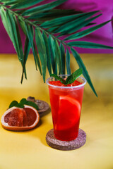 Red lemonade with grapefruit, ice and mint on tropical background