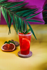 Red lemonade with grapefruit, ice and mint on tropical background