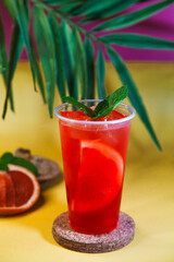 Red lemonade with grapefruit, ice and mint on tropical background