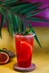 Red lemonade with grapefruit, ice and mint on tropical background