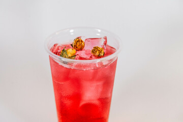 Red lemonade with ice and yellow rose buds on a white background.