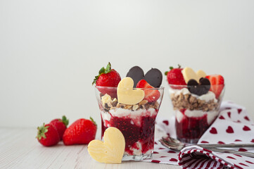 Two glasses with a sweet breakfast of cream cheese and pureed berries on a white wooden table. Side view. Strawberry valentine's day dessert decorated with heart-shaped chocolate and ripe berries