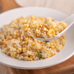 Eating Chinese fried rice in white plate on bright wooden table background.