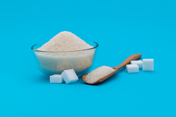 A bowl granulated sugar and sugar cubes on blue background