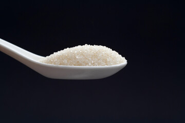 Ceramic spoon with sugar crystals on black background
