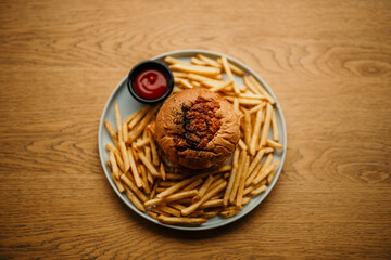 Top view of an isolated burger with ketchup and french fries served on a plate on a wooden table.