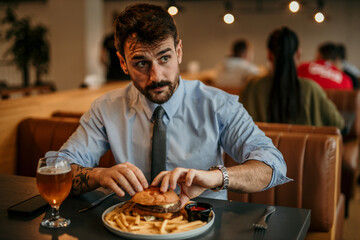 A handsome businessman in a blue shirt and tie sitting and about to have a burger for lunch in a pub during an office break.