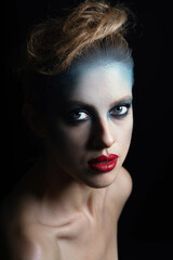 Fashion concept. Studio portrait of beautiful woman with fancy and futuristic blue, gray make-up and red lipstick. Model with blue eyes looking at camera with seductive look. Desaturated colors